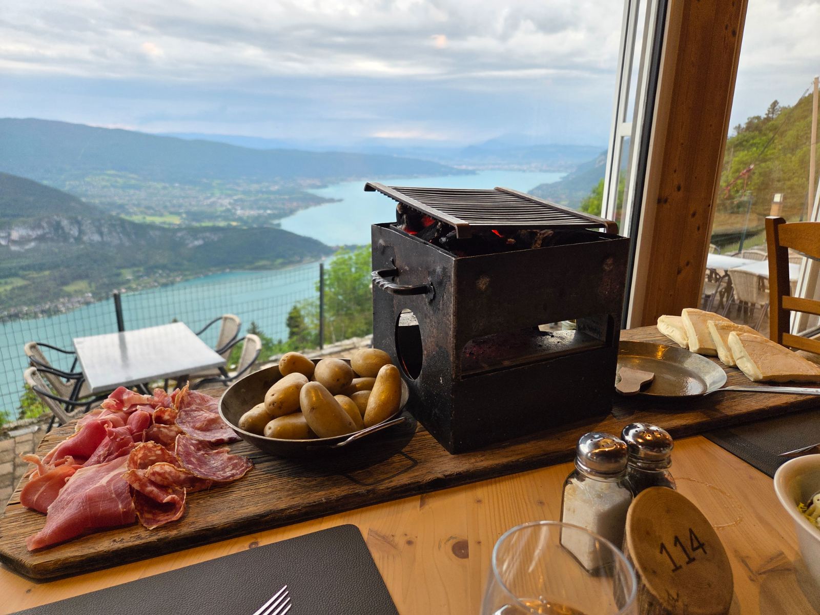 Raclette grill and charcuterie board at a mountain chalet table overlooking Lake Annecy