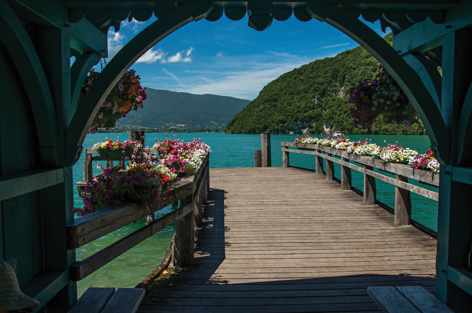 Covered wooden pier with flower boxes opening onto the turquoise lake near Talloires