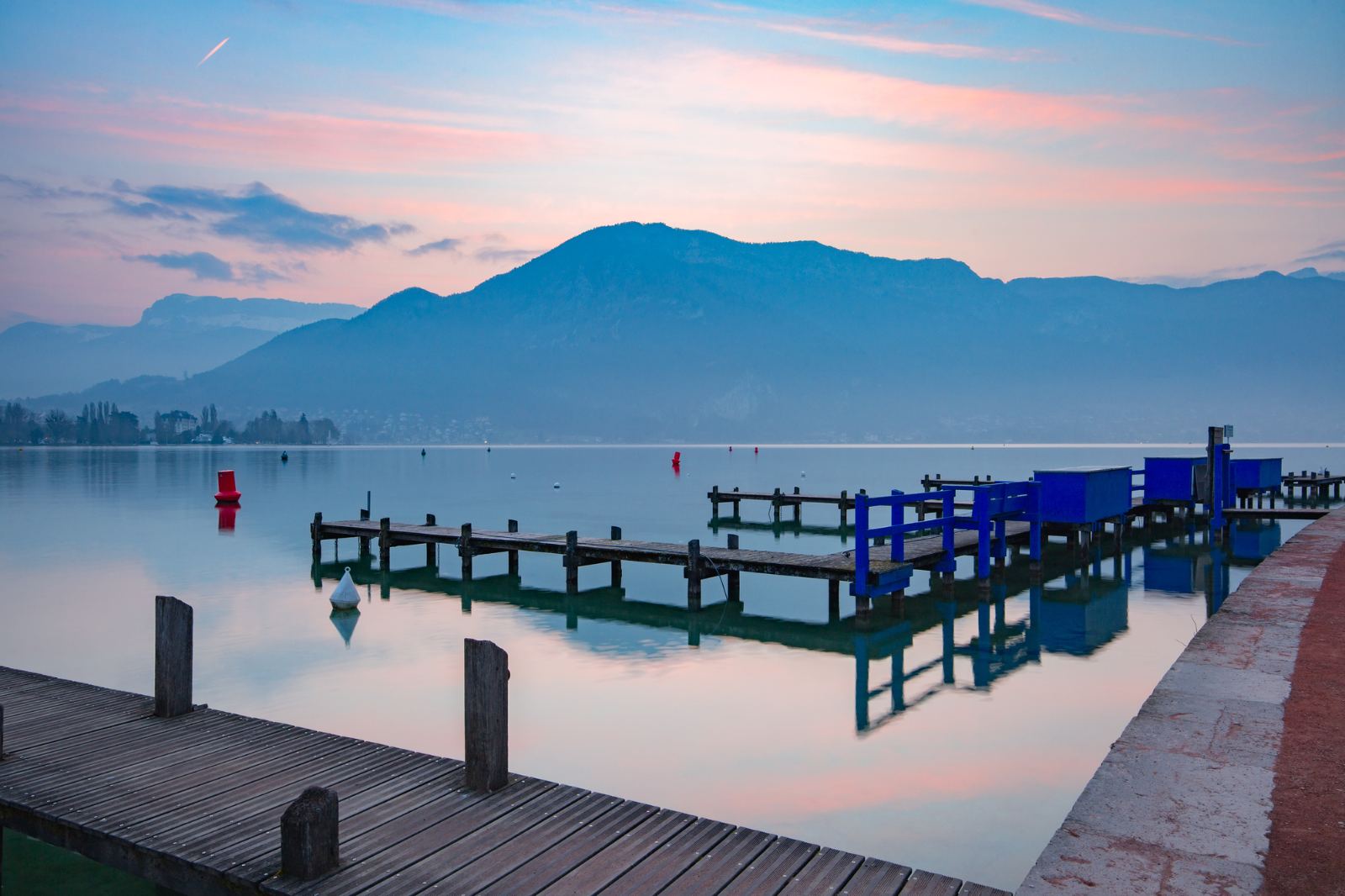 Pink and blue sunset over calm Lake Annecy with wooden piers and mountains