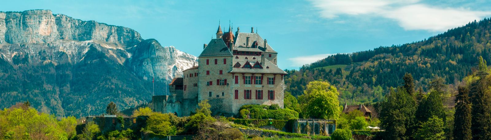 Menthon-Saint-Bernard castle above green gardens with limestone cliffs behind